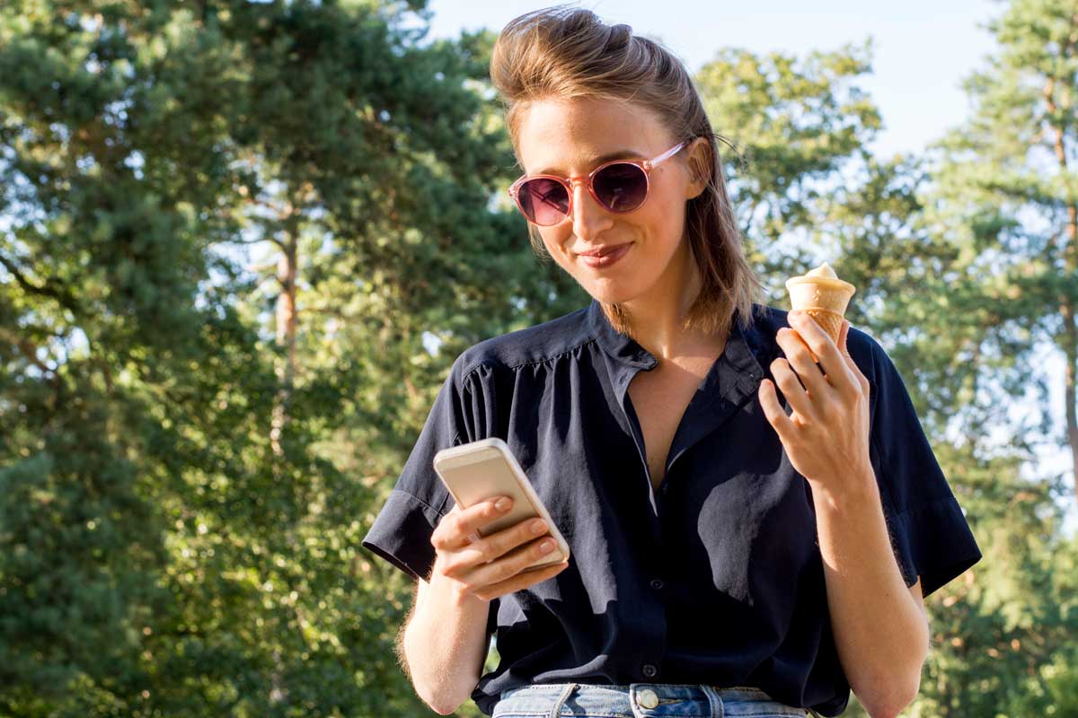 Kvinna som håller i en mobil och äter glass